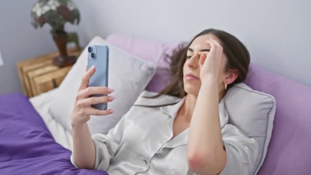 Νεαρή όμορφη ισπανόφωνη γυναίκα ξαπλωμένη στο κρεβάτι τελειώνει χρησιμοποιώντας το smartphone για να κοιμηθεί στο υπνοδωμάτιο - Πλάνα, βίντεο