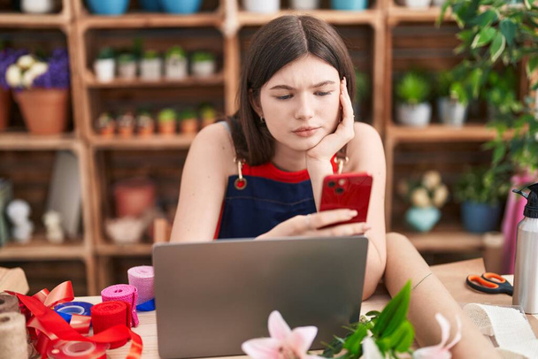 Giovane donna caucasica fiorista utilizzando smartphone e laptop al fiorista - Foto, immagini