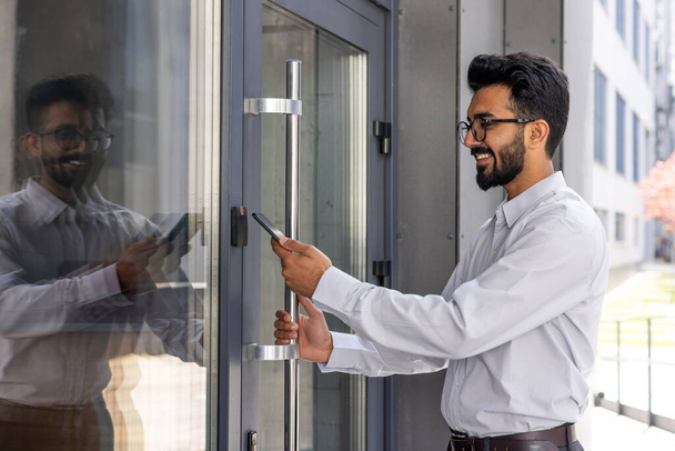 Young businessman using phone to open office door of building, man happy using wireless access, businessman going to work happy smiling. - Photo, Image