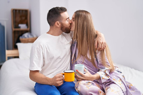 Man and woman couple kissing and hugging each other drinking coffee at bedroom - Foto, imagen