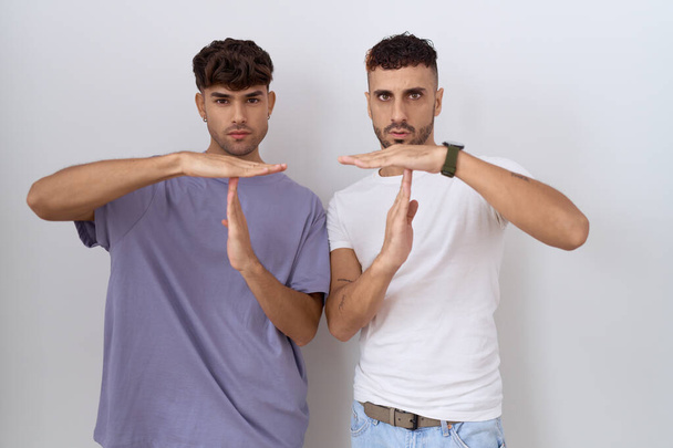 Гомосексуальна гей-пара, що стоїть над білим тлом, робить час жестом руками, розчарованим і серйозним обличчям  - Фото, зображення