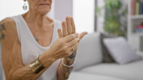 Старшая седовласая женщина, страдающая сильной болью в руке, сидящая дома на диване в гостиной, пожилая женщина с короткими волосами, выглядящая травмированной, проблемы с остеоартритом в помещении. - Фото, изображение