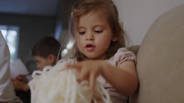 Egy kislány, aki zsinórral játszik a kanapén. Motoros készségek fejlesztése. - Felvétel, videó