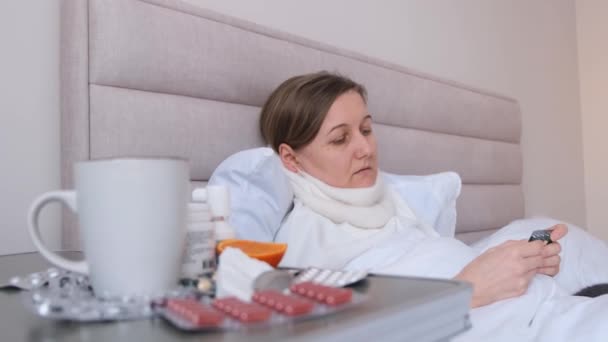 Žena, která má chřipku, léčí se s witaminy, léky, čajem, leží v posteli. Žena vypadá nemocná a unavená.. - Záběry, video