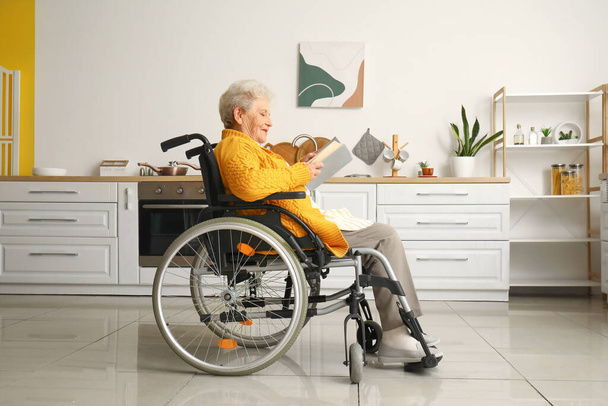 Oudere vrouw in rolstoel leesboek thuis - Foto, afbeelding