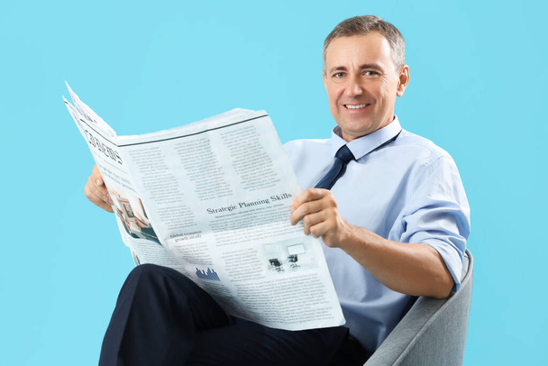 Ώριμος δημοσιογράφος με εφημερίδα σε πολυθρόνα σε μπλε φόντο - Φωτογραφία, εικόνα