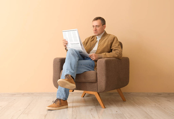 Mature journalist reading newspaper in armchair near beige wall - Photo, Image