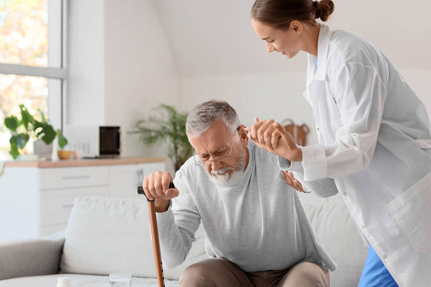 Enfermera ayudando a un hombre mayor a ponerse de pie en casa - Foto, imagen