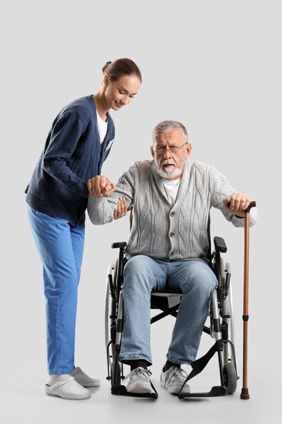 Ανώτερος άνδρας σε αναπηρική καρέκλα με νοσοκόμα σε ελαφρύ φόντο - Φωτογραφία, εικόνα