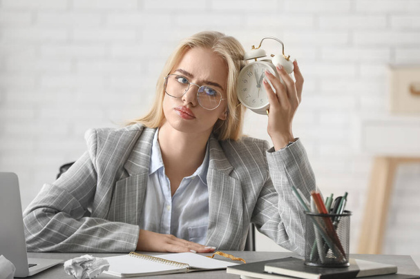 Young thoughtful businesswoman with alarm clock trying to meet deadline in office. Time management concept - Photo, Image