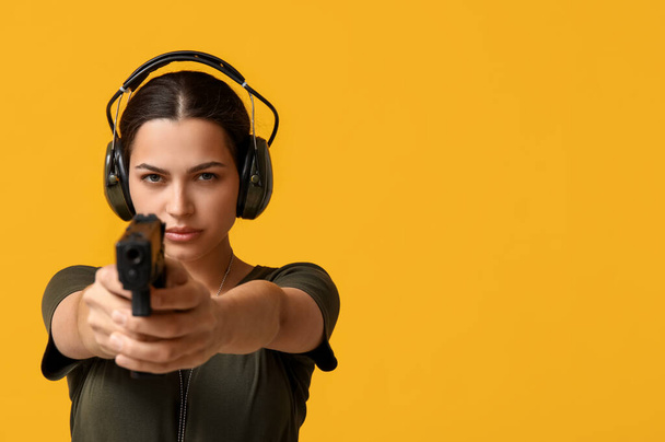 Confident young female soldier with handgun on yellow background, closeup - Photo, Image