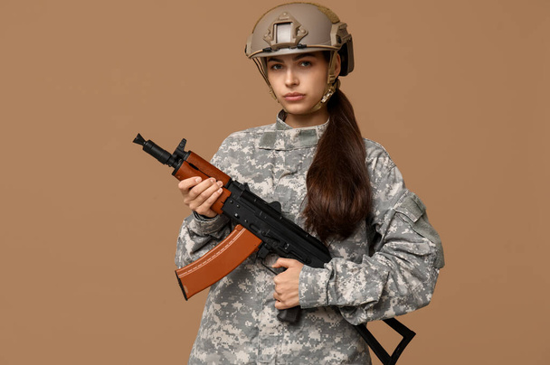 Pewna siebie młoda żołnierka z karabinem szturmowym na beżowym tle - Zdjęcie, obraz