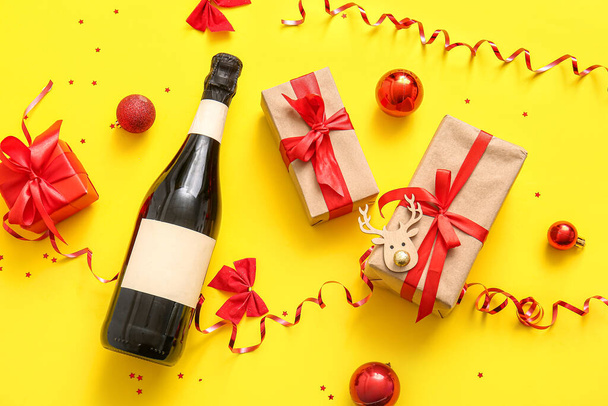 İçinde Noel topları olan bir şişe şampanya ve sarı arka planda hediye kutuları. - Fotoğraf, Görsel