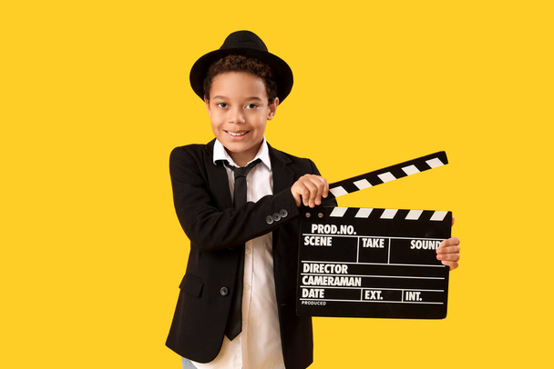 黄色の背景に映画のクラッパーボードを持つリトルアフリカ系アメリカ人の少年 - 写真・画像