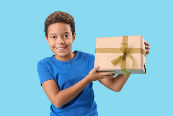 Pequeño niño afroamericano con caja de regalo sobre fondo azul - Foto, imagen