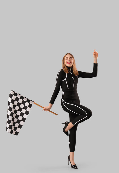Happy young woman with racing flag on grey background - Photo, Image