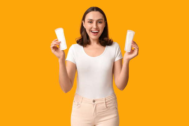 Beautiful young woman with menstrual pads on yellow background - Foto, Imagem