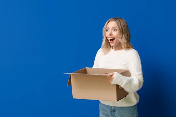 Jeune femme avec boîte ouverte en carton sur fond bleu - Photo, image