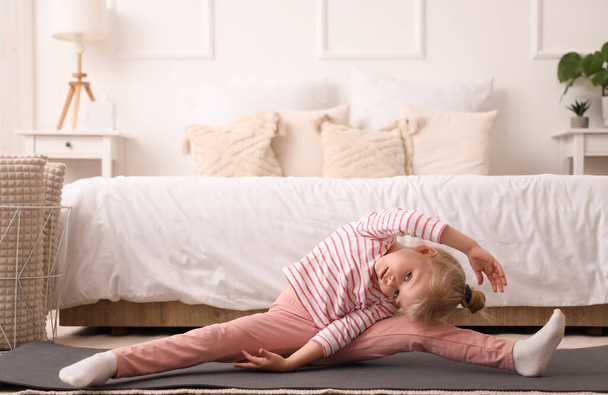 Roztomilá holčička dělá gymnastiku na podložce v ložnici - Fotografie, Obrázek