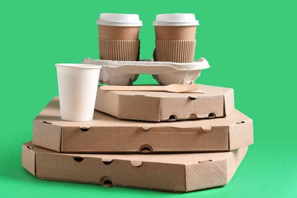 Бумажные чашки, столовые приборы и разные коробки для пиццы на зеленом фоне - Фото, изображение