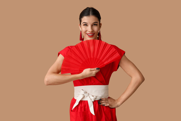 Beautiful young happy woman with fan on brown background. Chinese New Year celebration - Photo, Image