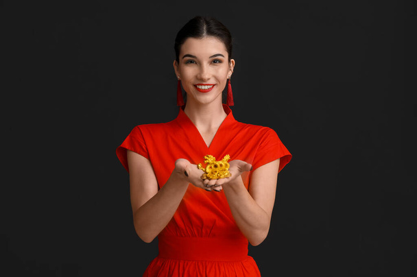 Beautiful young happy woman with golden dragon figurine on black background. Chinese New Year celebration - Photo, Image