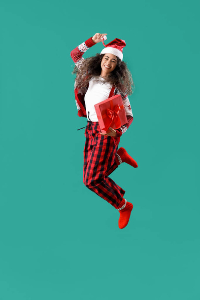 Mooie jonge gelukkig Afro-Amerikaanse vrouw in Santa hoed met geschenkdoos springen op groene achtergrond - Foto, afbeelding