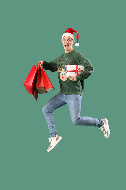 Knappe jonge gelukkig man met geschenkdozen en boodschappentassen springen op groene achtergrond - Foto, afbeelding