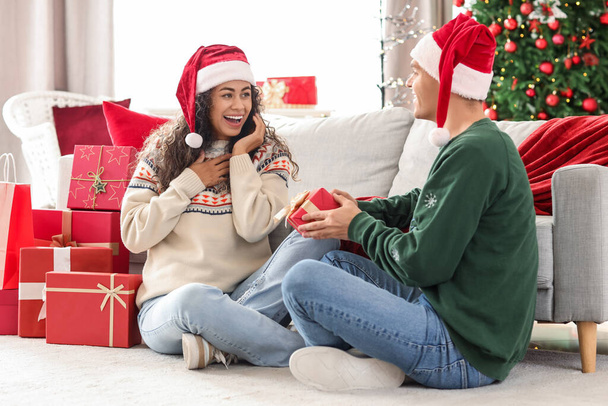 Joyeux jeune couple avec des boîtes-cadeaux assis dans la chambre décorée. Concept de shopping de Noël - Photo, image