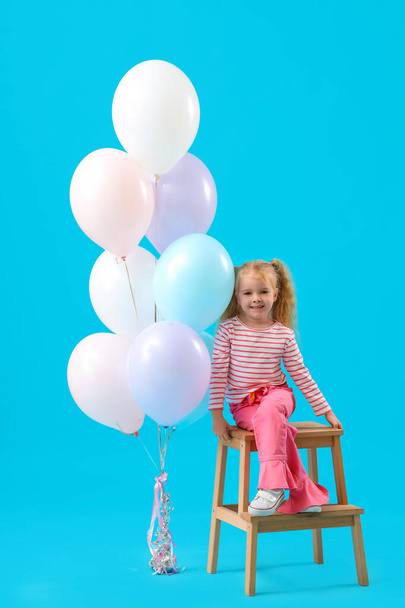 Милая маленькая девочка с красивыми воздушными шарами и стулом на голубом фоне - Фото, изображение