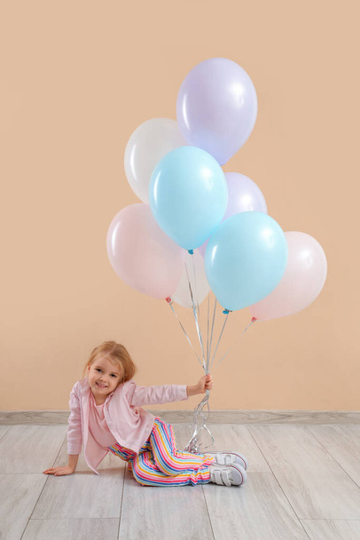 Cute little girl z pięknymi balonami siedzi w pobliżu beżowej ściany - Zdjęcie, obraz