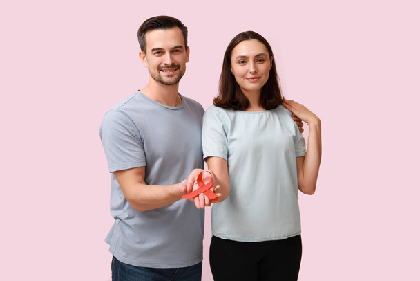 Preciosa pareja con cinta roja sobre fondo rosa. Concepto del Día Mundial del SIDA - Foto, imagen