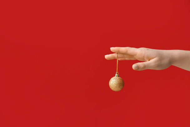 Mano femenina con bola de Navidad sobre fondo rojo - Foto, Imagen