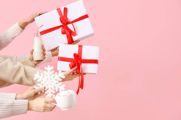 Ruce drží vánoční dárky, vločky, láhev mléka a hrnek s marshmallows na růžovém pozadí - Fotografie, Obrázek