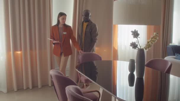 潜在的なバイヤーのツアーを与える家具店で働くオレンジのジャケットの白人女性の追跡ショット - 映像、動画