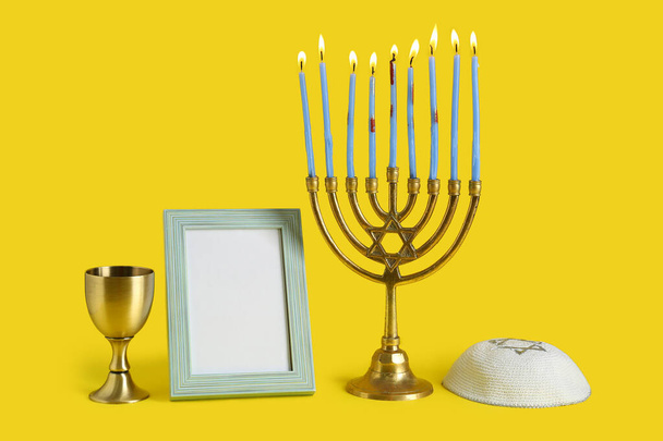 Menorah, kippah, marco de imagen en blanco y taza para la celebración de Hanukkah sobre fondo amarillo - Foto, imagen