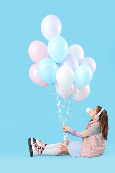 Trendy girl with balloons blowing bubble gum on blue background - Photo, Image