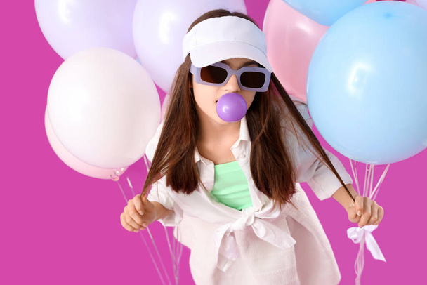 Fille à la mode avec des ballons soufflant gomme à bulles sur fond violet - Photo, image