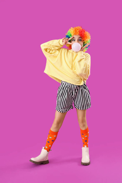 Trendy meisje in clown kostuum blazen kauwgom op paarse achtergrond - Foto, afbeelding