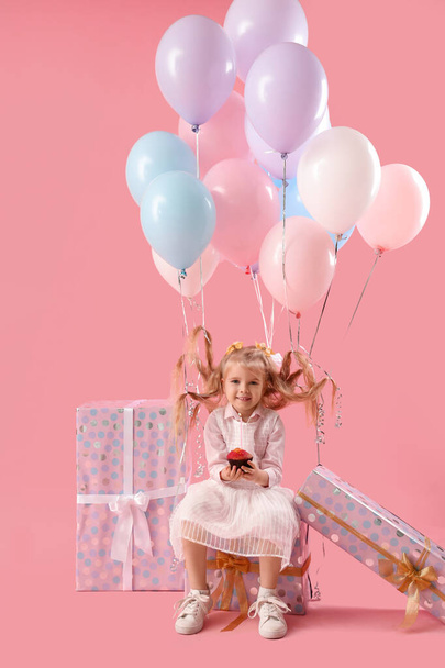 Söpö pieni tyttö syntymäpäivä muffini, ilmapalloja ja lahjoja vaaleanpunainen tausta - Valokuva, kuva
