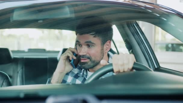 Молодий чоловік сидить у машині під час прокляття під час розмови по телефону. Транспорт, технології, концепція способу життя. Повільний рух - Кадри, відео