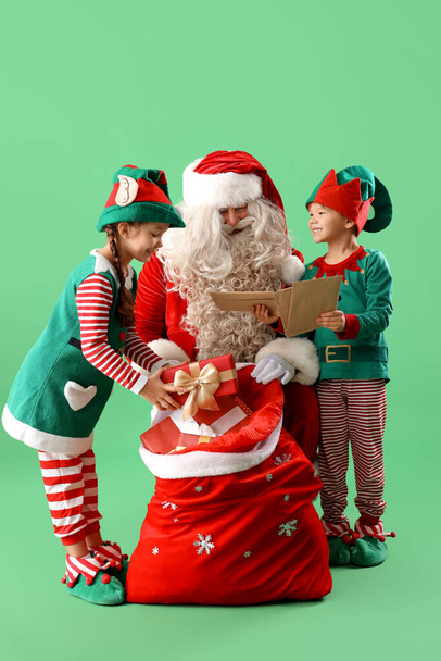 Little elves with letters and bag of gifts helping Santa Claus on green background - Photo, Image