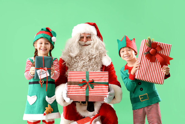 Małe elfy z Mikołajem i prezenty świąteczne na zielonym tle - Zdjęcie, obraz