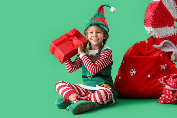 緑の背景にクリスマスギフトとサンタバッグでかわいい小さなエルフ - 写真・画像