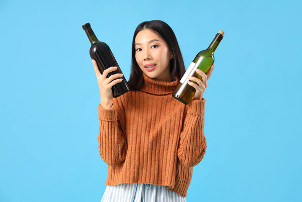 Hermosa mujer asiática con botellas de vino sobre fondo azul - Foto, imagen