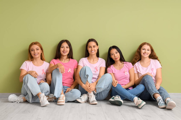 Mulheres bonitas com fitas rosa sentadas perto da parede verde. Conceito de consciência do câncer de mama - Foto, Imagem