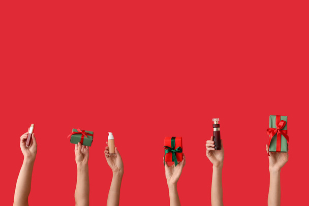 Dámské ruce s různými kosmetické výrobky a dárky na červeném pozadí - Fotografie, Obrázek