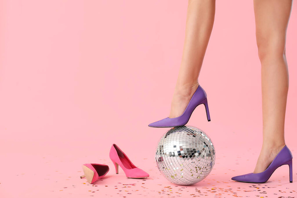 Female legs in stylish high heels with disco ball and confetti on pink background - Photo, Image