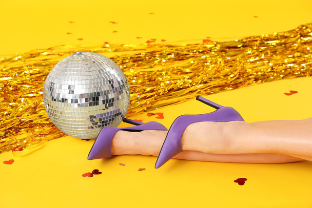 Жіночі ноги в стильних високих підборах з диско-кулькою і конфетті на жовтому тлі - Фото, зображення