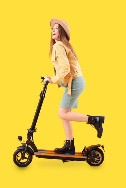 Beautiful young pregnant woman with electric kick scooter on yellow background - Photo, Image
